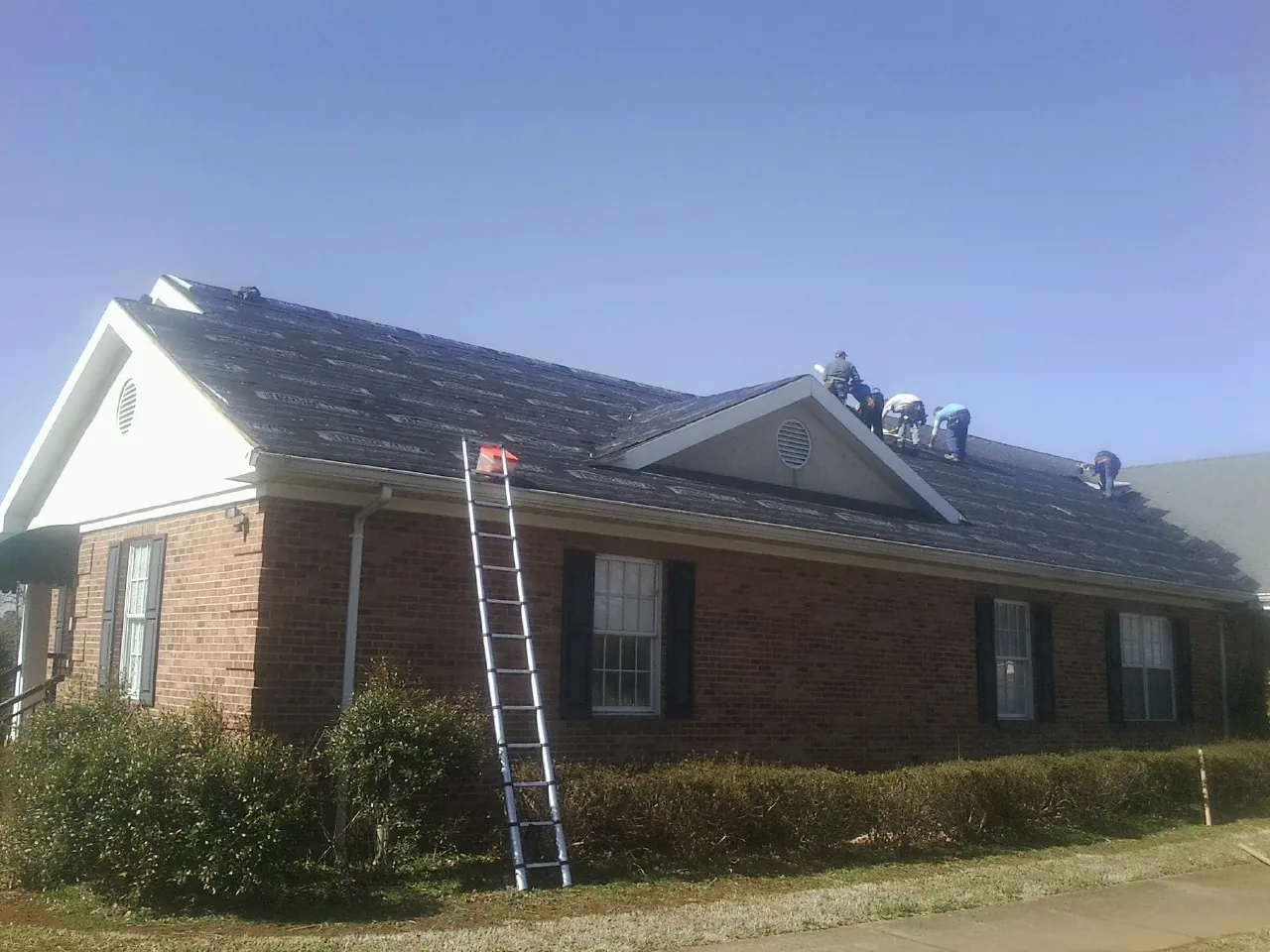 Crew tearing shingles off a brick ranch roof with a ladder set — Emergency Roof Repair work by our crew in Stockton
